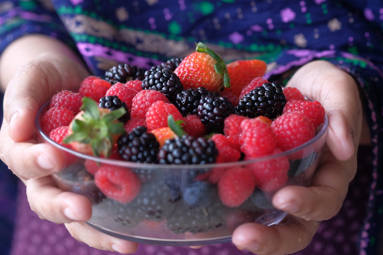 About Close-up of hands holding a glass bowl filled with fresh mixed berries.